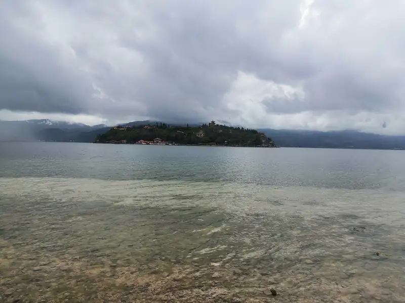 Clear shallows of Fuxian Lake and a small wooded island under a cloudy sky